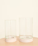 Two Stowe Eco Glass Vases with light wooden bases are side by side on a light wood surface, set against a plain cream background. One sustainable vase is slightly taller than the other.