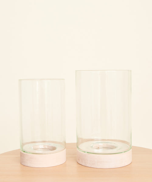 Two Stowe Eco Glass Vases with light wooden bases are side by side on a light wood surface, set against a plain cream background. One sustainable vase is slightly taller than the other.