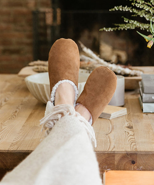 A person relaxes with their feet up, wearing Suede Moroccan Slippers that exude comfort and style.