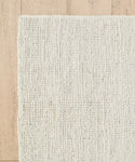 A close-up of the cream-colored Wilder Jute Rug on a light wooden floor, showcasing its handwoven texture, subtle pattern, and chunky fibers.
