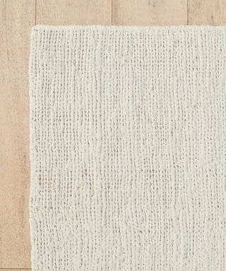 A close-up of the cream-colored Wilder Jute Rug on a light wooden floor, showcasing its handwoven texture, subtle pattern, and chunky fibers.