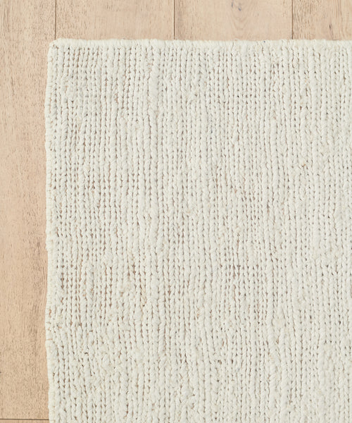 A close-up of the cream-colored Wilder Jute Rug on a light wooden floor, showcasing its handwoven texture, subtle pattern, and chunky fibers.