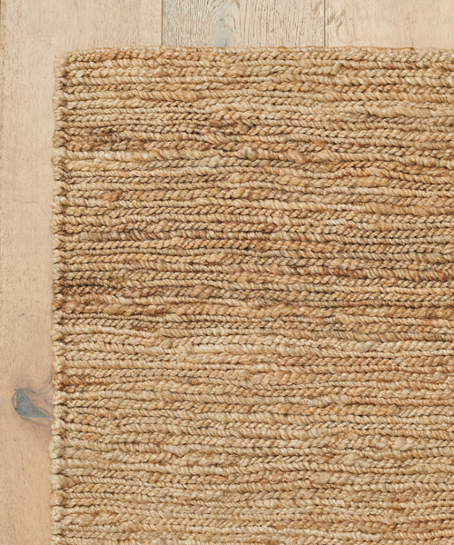 A close-up of the Wilder Jute Rug on a light wooden floor, highlighting its textured, natural fibers and intricate handwoven pattern.