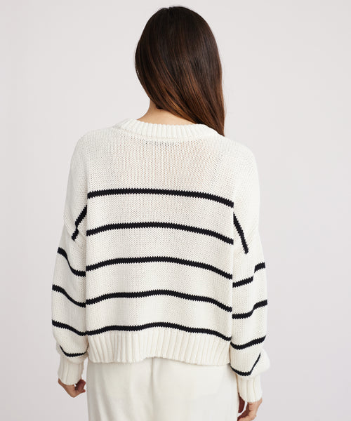 A person with long brown hair, seen from behind, wears the Chloe Crewneck—a loose-fitting black stripe sweater with ribbed cuffs—standing against a plain light background.