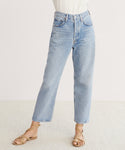 Person wearing AGOLDE 90s Crop Jean in light blue organic cotton denim, a white tucked-in top, and tan strappy sandals, standing against a plain light background. Only the lower body is visible.