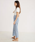 Woman in profile against a plain background, wearing a white short-sleeve top, 90s Crop Jean in light blue organic cotton denim by AGOLDE, and tan sandals.