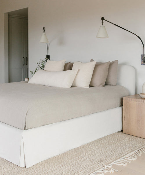 The Cove Bed features Belgian Libeco linen, plush pillows, a lamp, and a linen upholstered headboard—creating a serene and comfortable retreat.