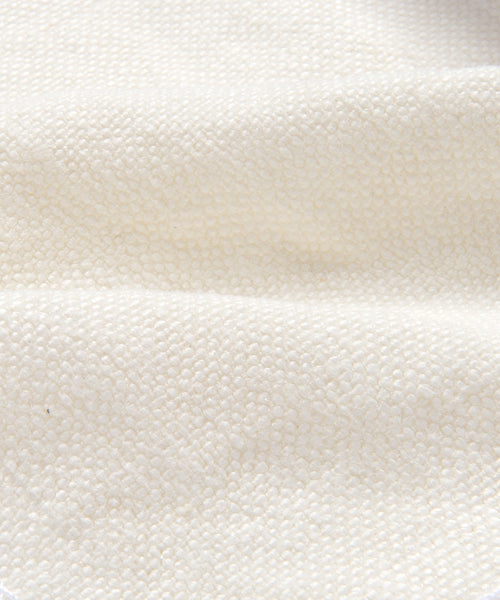 Close-up of the Cove Bed Slipcover, made from textured, off-white Belgian Libeco linen with a bumpy, pebble-like surface and soft folds.