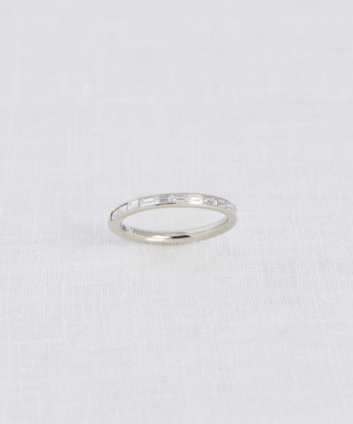 The June Baguette Band showcases slim rectangular-cut clear stones in a continuous row, photographed on white textured fabric—an elegant heirloom-inspired jewelry piece.