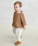 A young child with short light brown hair wears a Kids Fisherman Sweater, cream pants, and brown shoes, standing on a light textured floor against a neutral background.