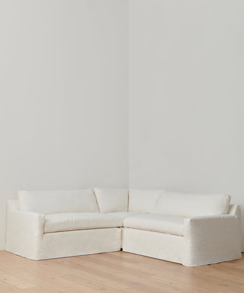The Harbor Sectional, in Belgian flax linen with plush cushions, sits in a corner on light wood floors and against white walls—a classic sofa choice for any room.