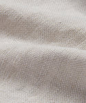Close-up of the Cove Bed Slipcover, featuring light beige Belgian Libeco linen with a textured, soft surface and visible weave. The fabric is gently draped, forming subtle folds and shadows.