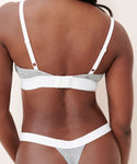 A person is shown from the back wearing the Whipped Triangle Bralette in grey and white with adjustable straps, paired with matching thong underwear. The image highlights the fit and design of the undergarments against their skin.