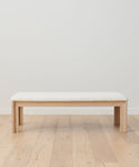 The Otto Bench showcases an Ivory Wool Boucle cushioned seat atop crisp White Oak, styled on a light wood floor with a plain white wall backdrop.