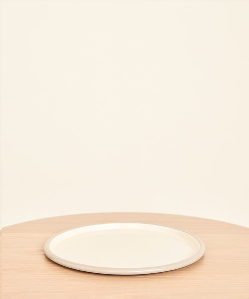 The Picnic Serving Platter from Crow Canyon, in plain white enamel, rests on a light wooden table set against a beige background. The minimal scene features only the platter with no food or other items present.