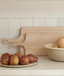 A kitchen counter featuring two wooden cutting boards, a plate of pears, a beige bowl with butternut squash, and a Picnic Serving Platter from Crow Canyon, set against a white tiled wall.