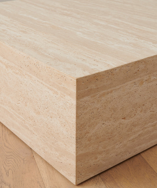 Close-up of the Sur Square Coffee Table’s corner on a wooden floor, showcasing the natural texture and linear patterns of its light beige travertine surface.