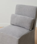 The Sunset Dining Chair Slipcover, in light gray ash linen, covers a modern armless chair and includes a rectangular matching lumbar pillow, shown against a white wall and wooden floor.