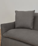 A close-up of the Miramar Sofa Slipcover in modern gray Belgian linen, paired with a matching square cushion, set against a plain white wall and light wooden floor.