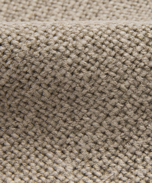 Close-up of the Sunset Dining Chair Slipcover in beige woven fabric. Its coarse, textured pattern and gentle folds add subtle elegance—perfect for enhancing any dining chair with a taupe linen look.