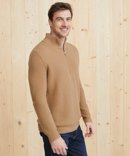 A smiling man in the Mens Wool Half Zip sweater and dark jeans stands before a light wooden wall, gazing slightly to the side.