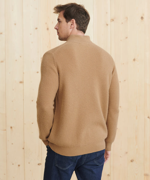 A man in a tan Mens Wool Half Zip and dark blue jeans stands with his back to the camera in front of a light wooden wall.